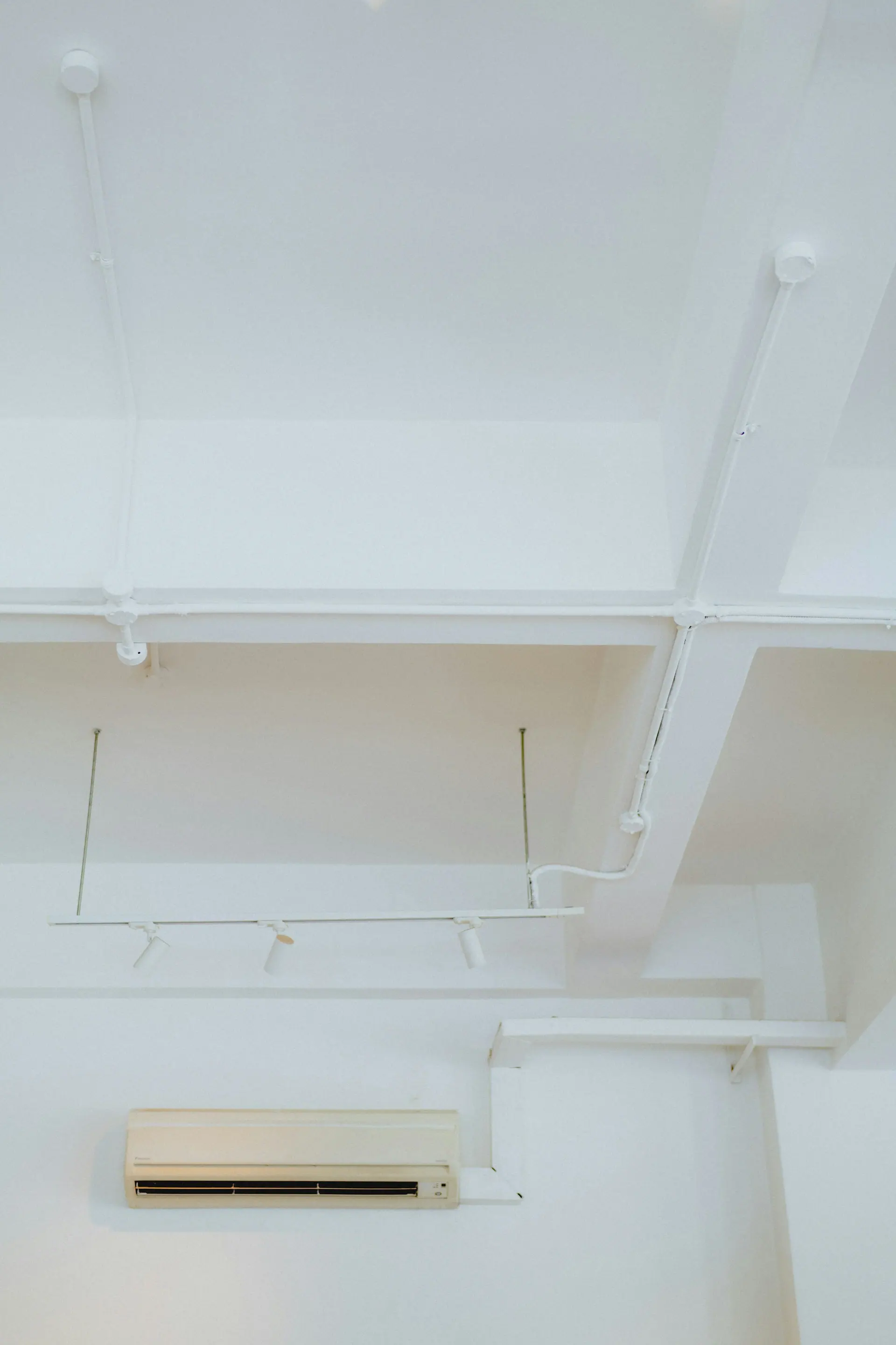 Split air conditioner mounted high on a white wall below exposed cable trunking