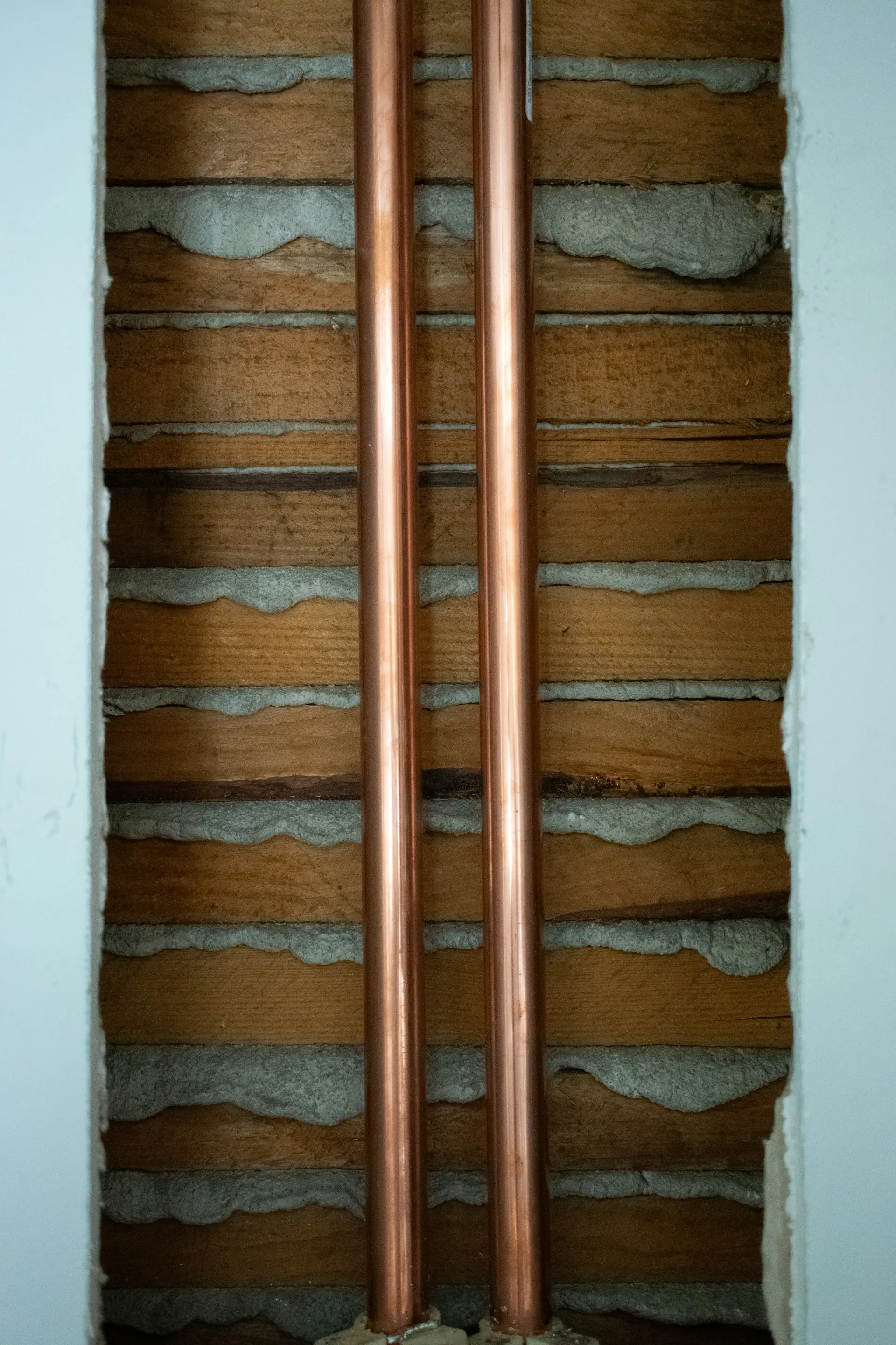 Pair of copper refrigerant pipes running down a wall