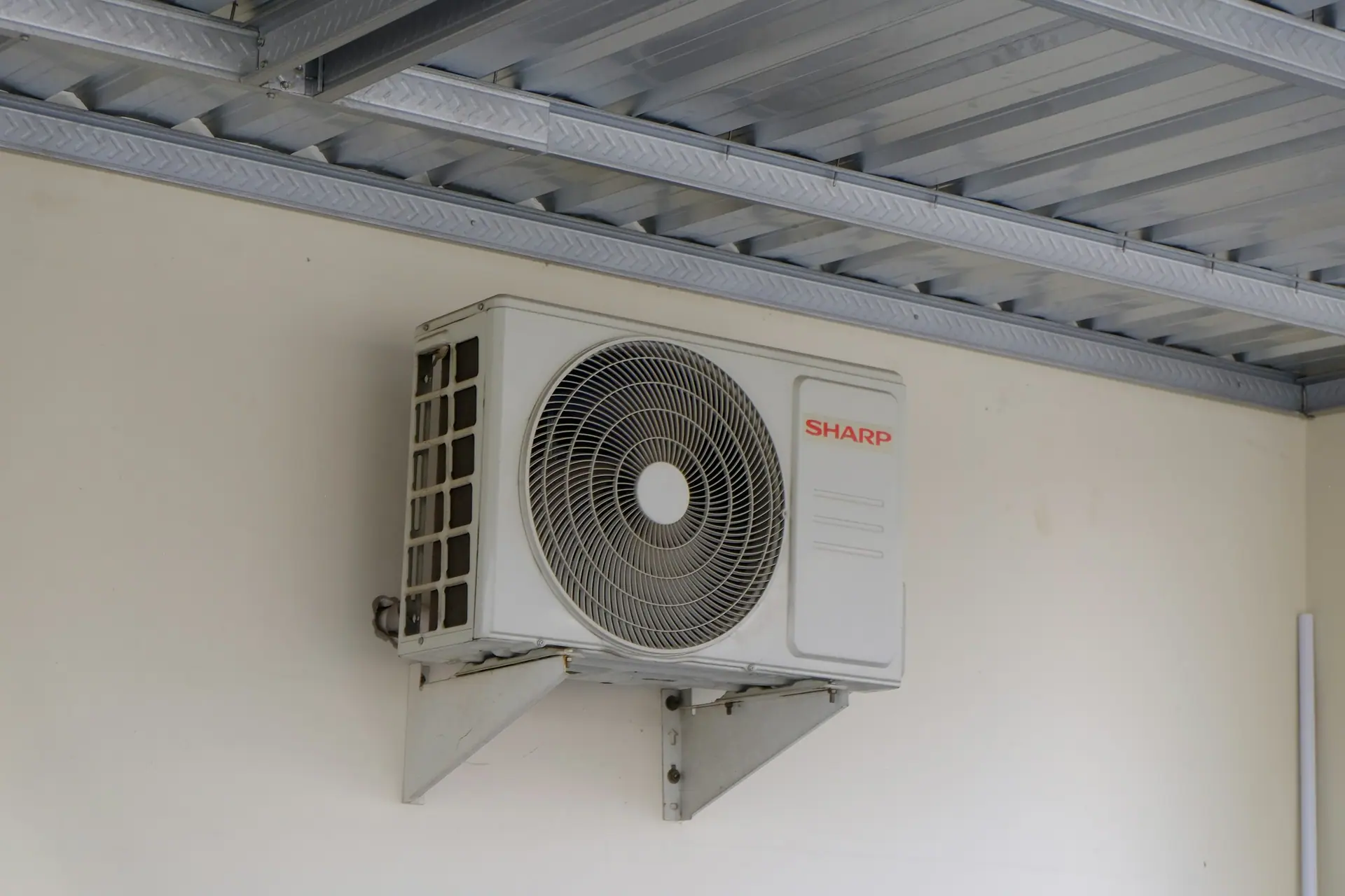 Outdoor air conditioning unit mounted on a wall bracket under a roof overhang